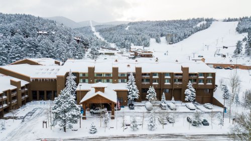 A snowy mountain resort with a lodge, surrounded by trees and ski slopes in the background.