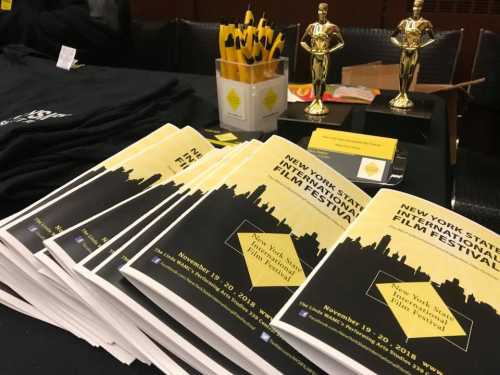 A table displaying brochures for the New York State Film Festival, along with pens, awards, and promotional materials.