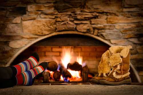 Cozy scene with colorful socks and warm boots in front of a crackling fireplace.