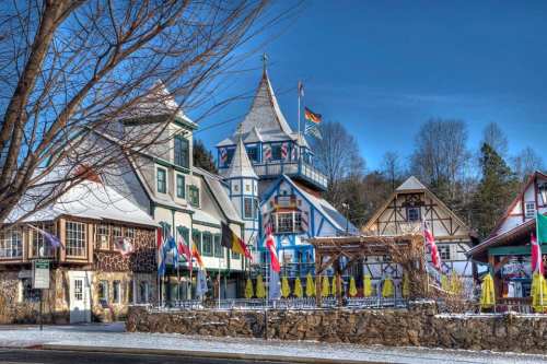 Charming alpine-style buildings with colorful facades and flags, set against a clear blue sky in a winter landscape.