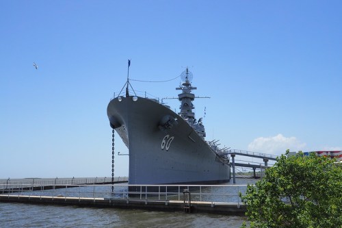 A large battleship docked by the water under a clear blue sky, with a walkway leading to its entrance.