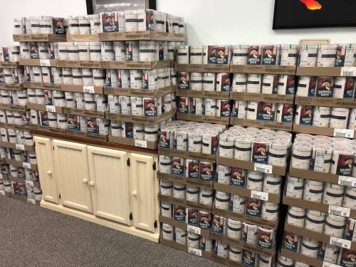 A large display of stacked paint cans in various colors, organized neatly on shelves and a cabinet.
