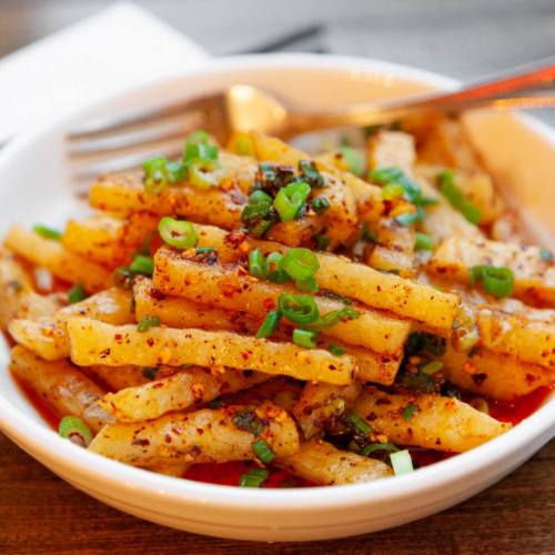 A bowl of spicy, seasoned potato sticks topped with chopped green onions.