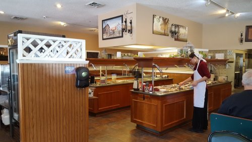 A restaurant buffet area with a server arranging food, featuring wooden decor and a cozy atmosphere.