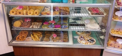 A display case filled with various colorful pastries and donuts, showcasing an assortment of sweet treats.