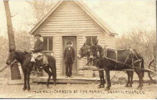 A historic photo of a mail carrier on horseback, with two horses and a man standing in front of a small house.