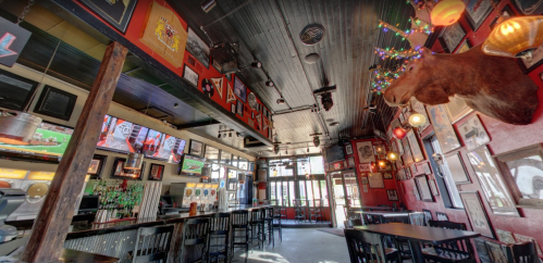 Interior of a lively bar with colorful decor, multiple TVs, and a moose head adorned with lights on the wall.