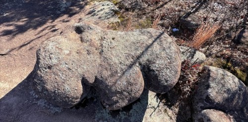 A large, weathered rock formation resembling a heart shape, surrounded by sparse vegetation and rocky terrain.