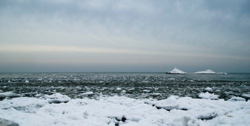 A serene winter landscape featuring a frozen shoreline and distant ice formations on a calm, gray sea.