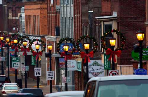 Street view decorated for the holidays, featuring wreaths and bows on lamp posts, with shops lining the road.