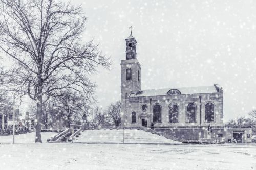 A snowy scene featuring a church with a tall clock tower, surrounded by bare trees and a serene winter landscape.