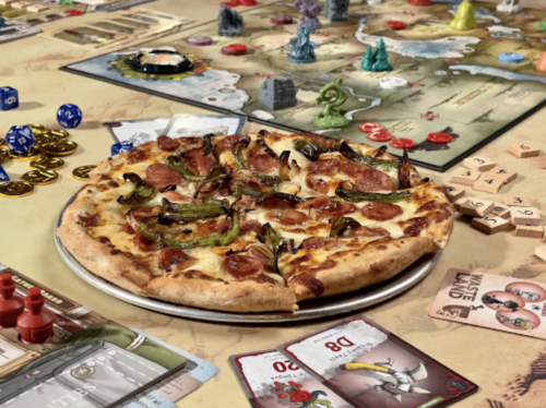 A pizza with pepperoni and green peppers on a table with various board game pieces and cards scattered around.