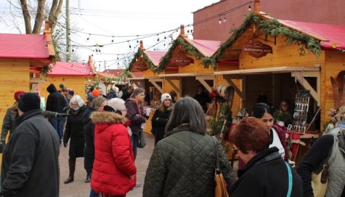 A bustling holiday market with wooden stalls, festive decorations, and crowds of people enjoying the atmosphere.