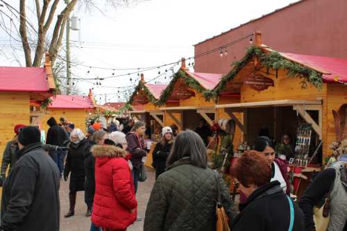 Crowd at a festive market with wooden stalls decorated for the holidays, people browsing and enjoying the atmosphere.