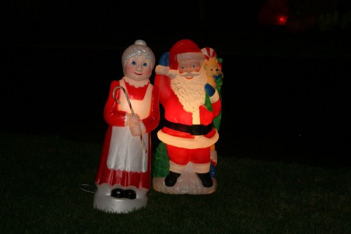A cheerful Santa Claus and Mrs. Claus lawn decorations, illuminated at night, standing on green grass.