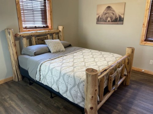 A rustic bedroom featuring a log bed with a patterned blanket and a bear-themed wall art above.