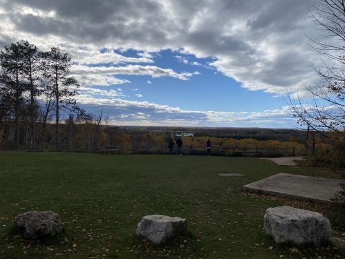 A scenic view from a park with people looking out over a valley under a partly cloudy sky.