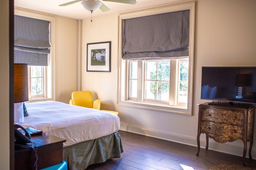 Bright hotel room featuring a bed, yellow chair, TV, and large windows with natural light.