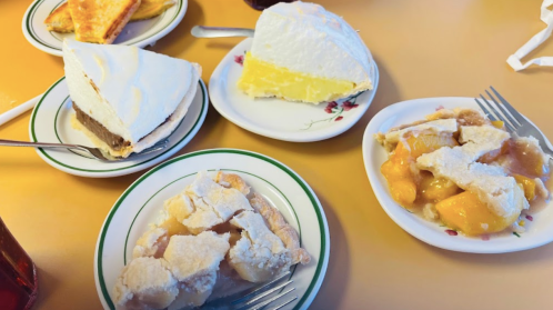 A table with four slices of pie: lemon, chocolate, and two servings of peach cobbler on white plates.