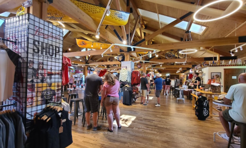 A vibrant retail store interior with customers browsing clothing and gear, featuring wooden beams and bright displays.