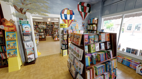 A cozy bookstore with colorful bookshelves, hot air balloons on the walls, and a welcoming reading area.
