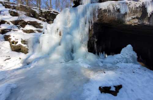 A frozen waterfall surrounded by snow and ice, with rocky formations in a winter landscape.