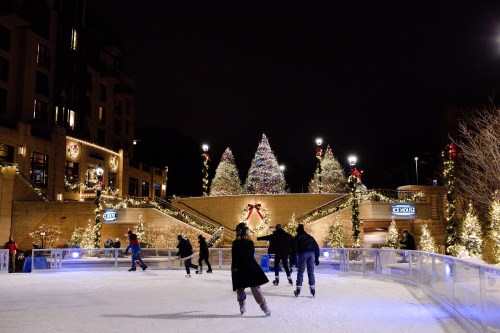 A festive outdoor ice skating rink surrounded by decorated trees and holiday lights at night.