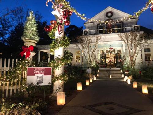 A festive house decorated for Christmas, featuring lights, wreaths, and candy canes, with luminaries lining the path.