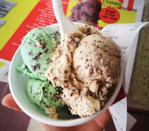 A hand holding a cup of ice cream with mint chocolate chip and cookies and cream flavors, with a receipt in the background.