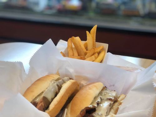 Two sandwiches with meat and sauce, served with a side of golden French fries in a paper container.