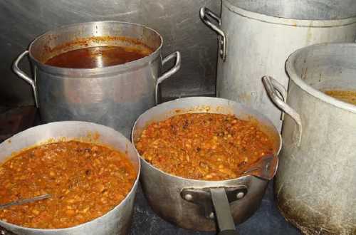 Three large pots of simmering stew and sauce on a stove, with one pot containing a thick, chunky mixture.