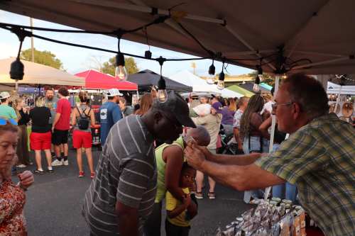 A busy market scene with people browsing stalls under tents, interacting and enjoying the atmosphere.
