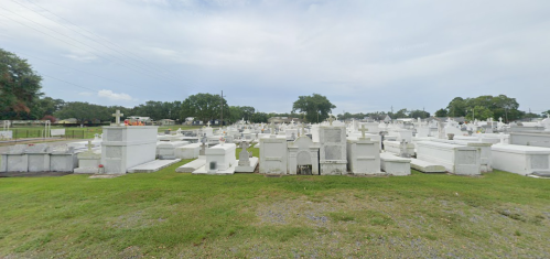A wide view of a cemetery with numerous white tombstones and crosses set against a cloudy sky.