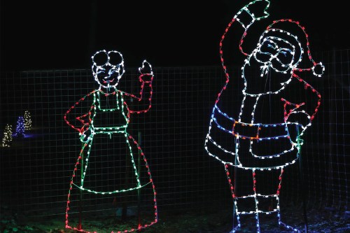 Colorful holiday lights depict a cheerful Santa and a woman waving, set against a dark background.