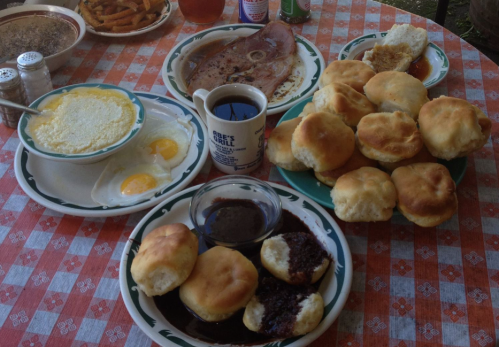 A table set with a hearty breakfast, featuring eggs, biscuits, ham, and coffee on a checkered tablecloth.