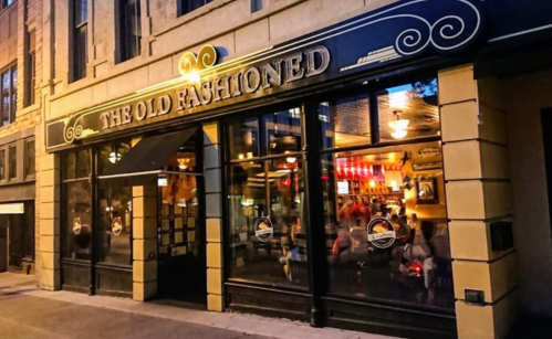 Exterior of "The Old Fashioned" restaurant, featuring large windows and a warm, inviting atmosphere at dusk.