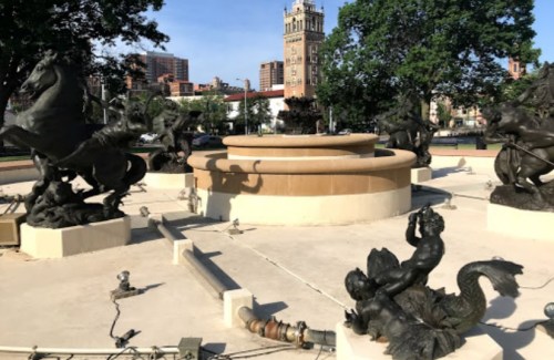 A fountain surrounded by bronze sculptures of horses and mythical figures in a park setting.
