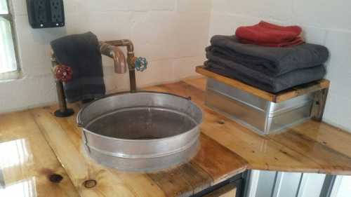 A rustic wooden countertop with a metal basin, faucet, and neatly stacked towels in gray and red.