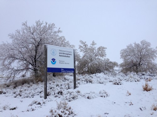 A snowy landscape featuring a sign for the National Oceanic and Atmospheric Administration amidst frosted trees.