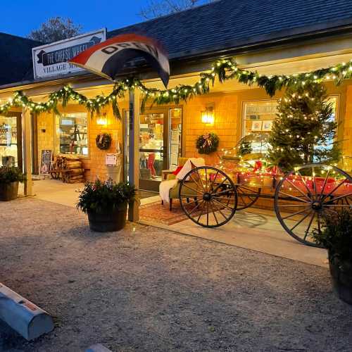 A charming shop exterior decorated with lights and holiday decor, featuring a wagon wheel and potted plants.