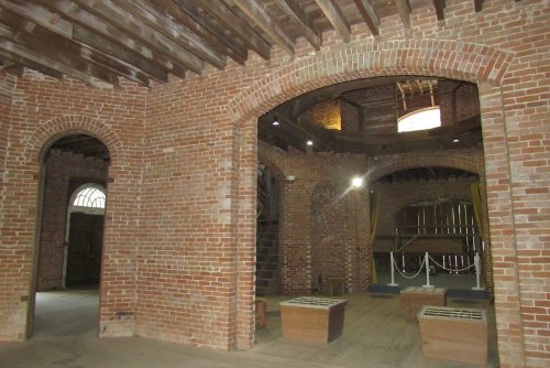 Interior of a brick building featuring arched doorways, wooden beams, and empty wooden boxes on the floor.