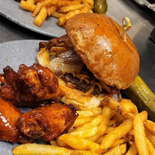 A plate featuring a burger with toppings, crispy fries, pickles, and chicken wings.