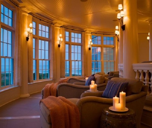 Cozy lounge area with soft lighting, comfortable chairs, and candles, overlooking a scenic view through large windows.