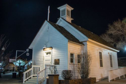 A small white historic building with a steeple, illuminated at night, surrounded by trees and streetlights.