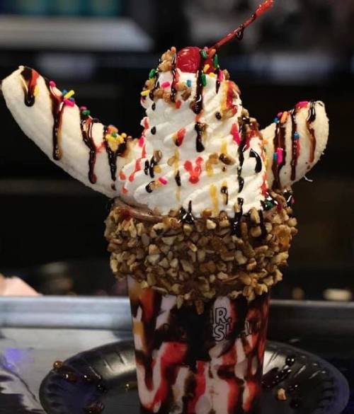 A decadent ice cream sundae topped with whipped cream, a cherry, banana slices, chocolate syrup, and sprinkles.