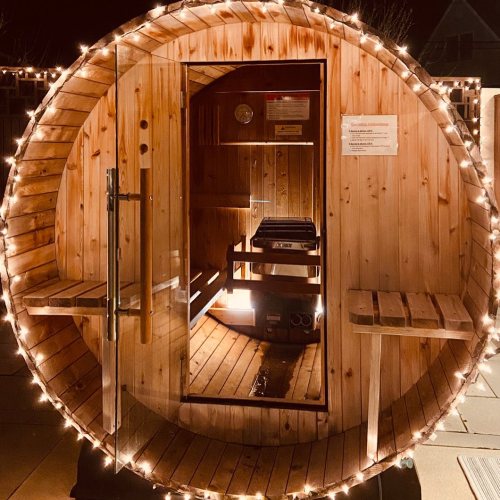 A wooden sauna with a circular design, illuminated by string lights, inviting and cozy at night.