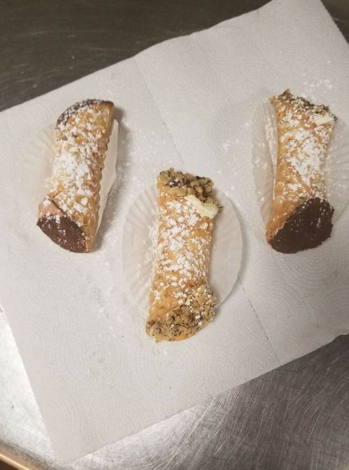 Three cannoli on paper plates, dusted with powdered sugar, resting on a countertop.