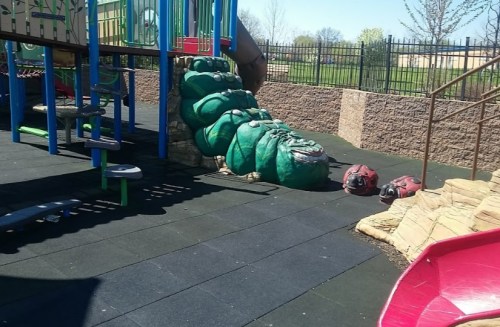 A playground featuring a green slide shaped like a caterpillar, with climbing structures and rubber flooring.