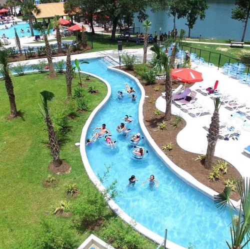 Aerial view of a lazy river pool with people floating, surrounded by palm trees and lounge chairs.