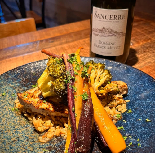 A plate of grilled chicken with colorful roasted vegetables and rice, alongside a bottle of Sancerre wine.